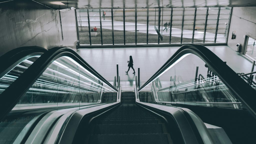 People using the sleek modern escalator in an indoor building with glass panels.